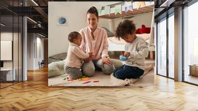 Single mother is sitting on the floor and playing with her small kids Wall mural