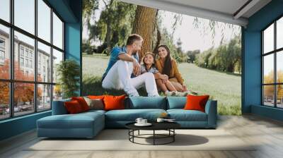 Smiling family is having rest on grass Wall mural