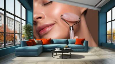 Smiling woman using face roller on her cheek Wall mural