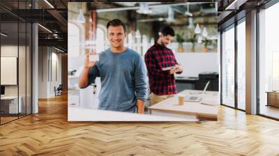 Waist up of a joyful young man standing in the office while showing his personal card Wall mural