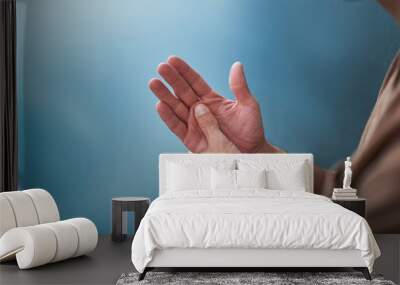 Young man rubbing palm by thumb on blue background Wall mural