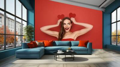 Young pretty girl imitating bunny ears by Valentines cards on red background Wall mural