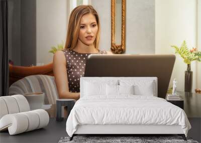 Young beautiful brunette woman works on laptop in cafe Wall mural