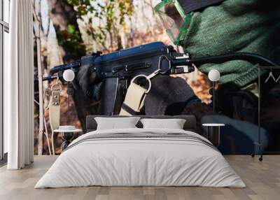 A soldier in a mask and with a weapon in his hands. Using an automatic rifle in the forest. Wall mural