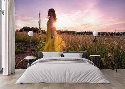 An Asian woman with long hair and yellow dress dances, rejoices, laughs under sunset with sunstar / sunburst Wall mural