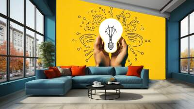 Two hands protecting yellow creative glowing light bulb against patent and problem solution ideas and creative thinking concept. Wall mural