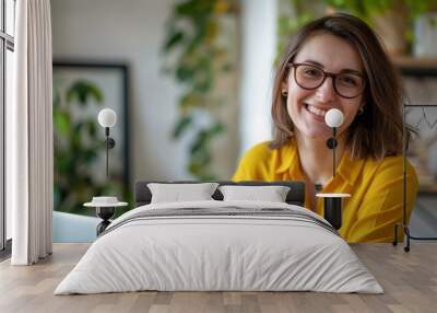 A woman in a yellow shirt is smiling and sitting in front of a laptop Wall mural