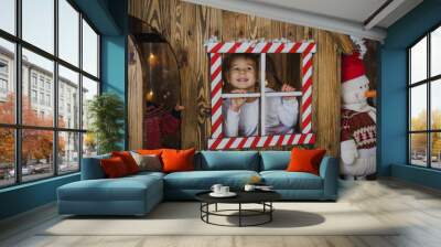 Funny little toddler girl peeping out the window playing with snow. Children play outside in the winter. Children have fun at Christmas. Children play building a snowman for Christmas. Photo studio Wall mural