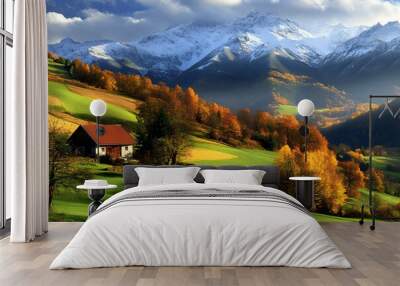 A cozy cabin sits amidst brilliant autumn foliage, surrounded by lush green fields with majestic snow-capped mountains rising in the background under a clear afternoon sky Wall mural