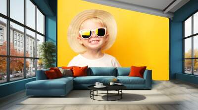 Portrait of a cute blond baby boy with a happy face smile in a straw hat and sunglasses on a yellow background looking at the camera. card with place for text Wall mural