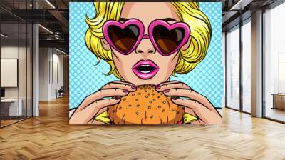 Vector color pop art comic style illustration of a girl eating a cheeseburger. Beautiful business woman holding a big hamburger. Successful young lady with open mouth bites a huge burger Wall mural