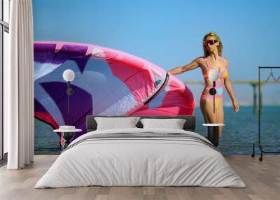 Kite surfing girl with blond hair in sun glasses in sexy pink bikini swimsuit with kite in the blue sea. Recreational activity, water sports, action, hobby, fitness in summer time. Kiteboarding sport Wall mural