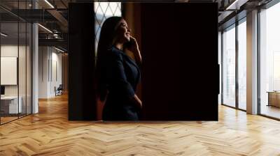 Smiling business woman making a phone call with her smartphone. Dressed in a blue suit. Standing on black background Wall mural