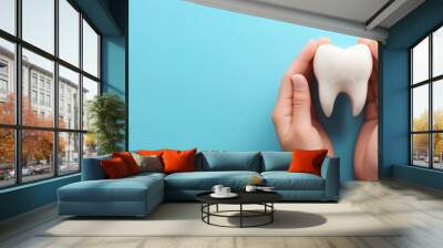 Concept of dental health, with a blue background and a model of teeth protected by both hands. The teeth stand larger than the palm of the hand, and the palm is protected on both sides of the teeth Wall mural