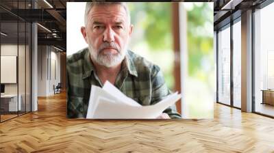 Man sitting at desk with concerned expression, holding stack of papers symbolizing financial stress and national debt, emphasizing personal and economic challenges. Wall mural