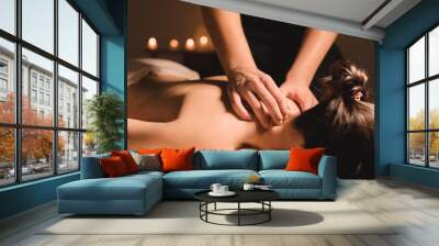 Men's hands make a therapeutic neck massage for a girl lying on a massage couch in a massage spa with dark lighting. Close-up. Dark Key Wall mural