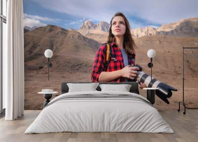 Young attractive caucasian woman with a professional photo camera in her hands against the backdrop of epic high rocks high in the caucasus mountains. Photo tours and landscape photography Wall mural