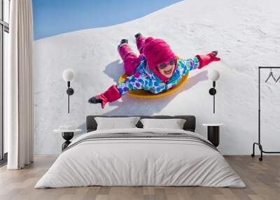 little girl riding on snow slides in winter time Wall mural