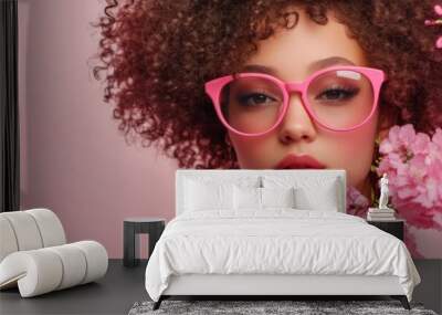 Young Woman in Pink Glasses and Curly Hair Holding a Pink Flower, Posing Before a Soft Pink Background,Beauty advertising poster background, 4K wallpaper Wall mural