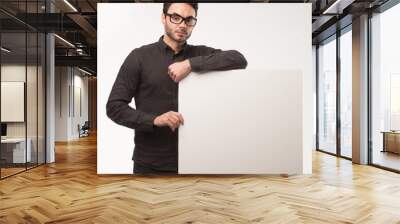 Young happy man showing presentation, pointing on placard over gray background Wall mural