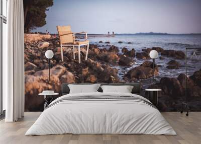 Wicker chair on rocky beach during sunset. Wall mural