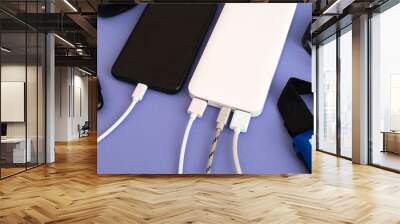 Smartphone and gadgets charging with power bank on purple background. A set of different gadgets: a flashlight, an electronic clock and a phone. Wall mural