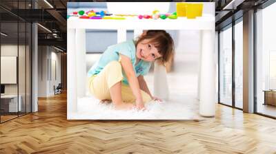 Little cute girl crawled under the table. The kid smiles, plays hide and seek Wall mural