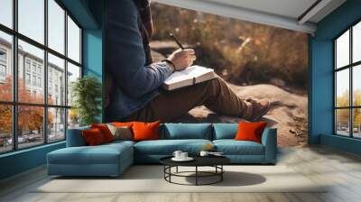 Person hands writing in a journal sitting at mountain rocks on ground. Earth Day Wall mural