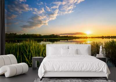 Amazing view at scenic landscape on a beautiful lake and colorful sunset with reflection on water surface among green reeds and glow on a background, spring season landscape Wall mural