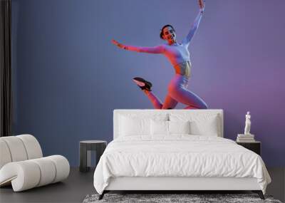 Athletic active woman jumping on studio background with colored filter. Dynamic movement Wall mural