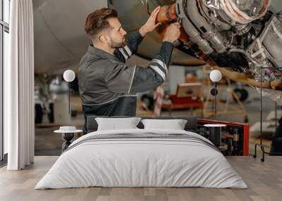 Bearded man maintenance technician tightening bolt with wrench while repairing airplane at repair station Wall mural