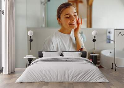 Beautiful young woman applying cosmetic serum onto her face in bathroom. Facial Skincare Wall mural