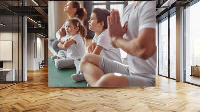 Calm woman is enjoying practice with husband and children and expressing namaste sign in lotus position Wall mural