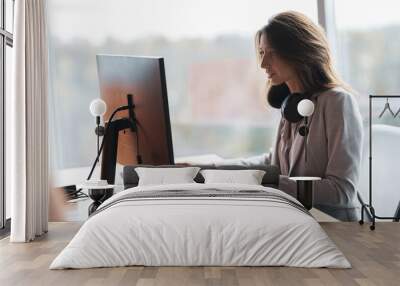 Focused businesswoman with headphones working on computer at workplace in modern office Wall mural