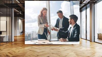 Positive office employees discussing work issues using laptop and documents with graphs and charts in a modern office. Teamwork concept Wall mural