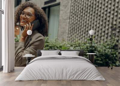 Pretty female freelancer is talking phone with client while standing on coworking background Wall mural