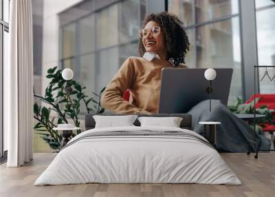 Pretty female freelancer working on laptop while sitting on modern coworking background Wall mural