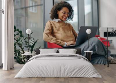 Pretty female freelancer working on laptop while sitting on modern coworking background Wall mural