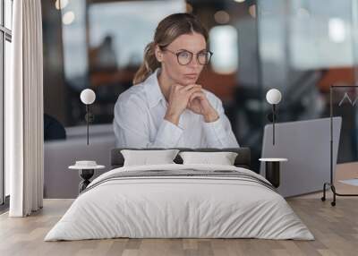 Serious businesswoman with glasses working on laptop at her workplace in modern office.  Wall mural