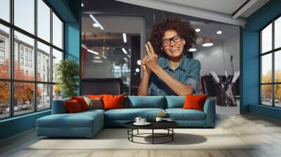 Smiling African American lady talking with sign language while sitting at her workplace in the office Wall mural