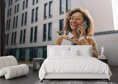 smiling woman manager is talking phone while standing with laptop on modern building background Wall mural