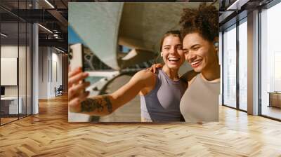 Two smiling female friends making selfie on a smart phone after morning run outdoors Wall mural