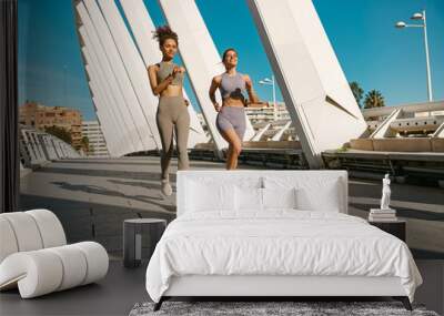 Two young women in sportswear are running on modern buildings background. Active lifestyle concept Wall mural