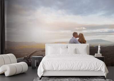 Young couple in love kissing near convertible car at roadside with romantic sunset. Rear concept Wall mural