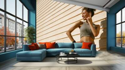 Young female athlete in sportswear have a rest after morning jogging outside and listen music Wall mural