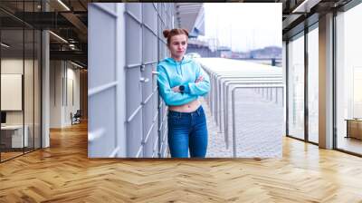 Girl in a blue crop top. Stylish streetwear for teens. Shooting near the gray grid. Blue jeans. Wall mural