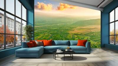 scenic rustic landscape with green hills and farms in a mountain valley during colorful cloudy sunset Wall mural