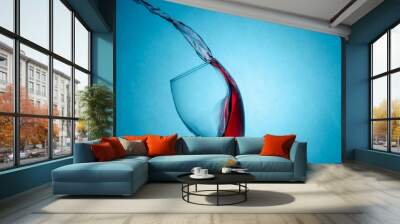 Beautiful splashes, drops of red wine in a glass on a blue background close-up with copy space. Freezing liquids in motion Wall mural