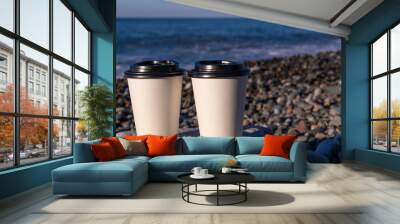 Close-up of two white paper cups standing on a stone by the sea on a sunny day, copy the space. Coffee to go Wall mural