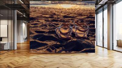 Leather sandals lie on the sand on the beach near the sea at sunset with copy space. Beautiful background on the theme of travel, beach holidays Wall mural